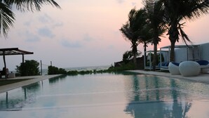 A swimming pool with a view of the ocean, surrounded by palm trees and lounge chairs.