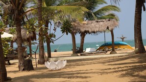 A beach with palm trees, a thatched-roof hut, and a blue umbrella.