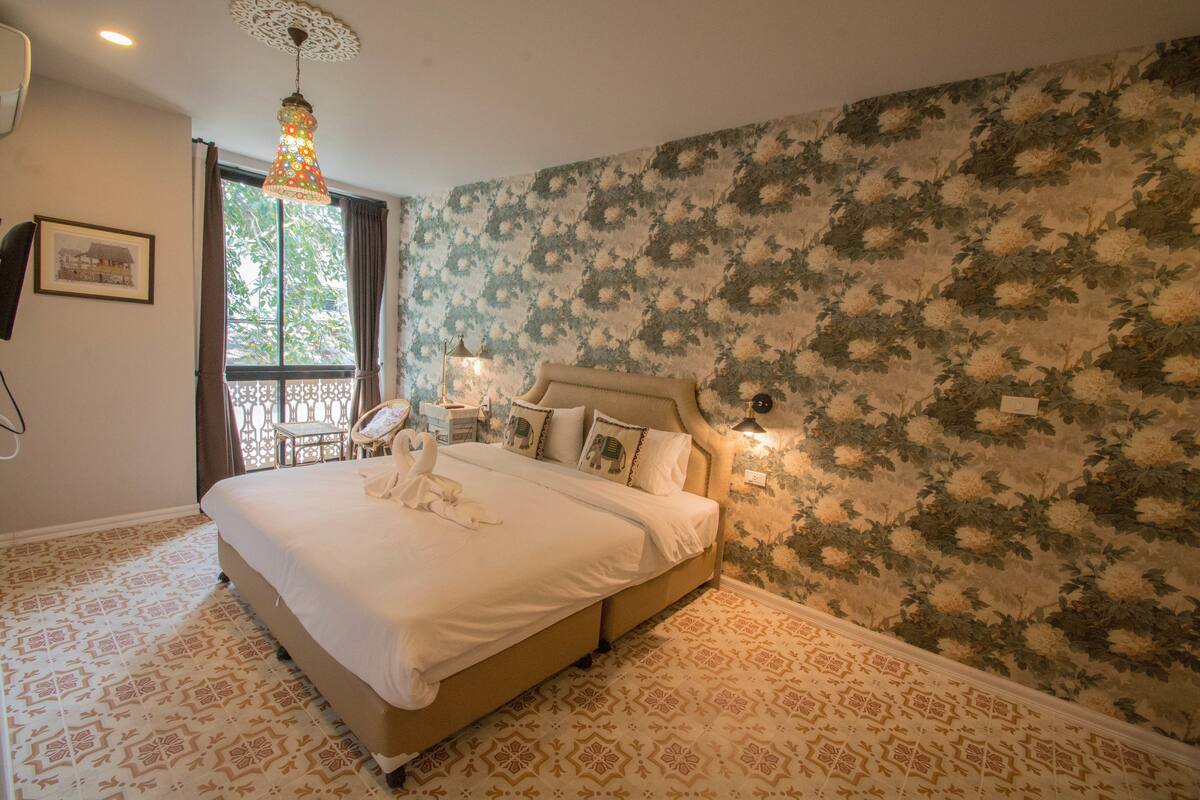 A bedroom with a large bed, floral wallpaper, and a patterned floor.