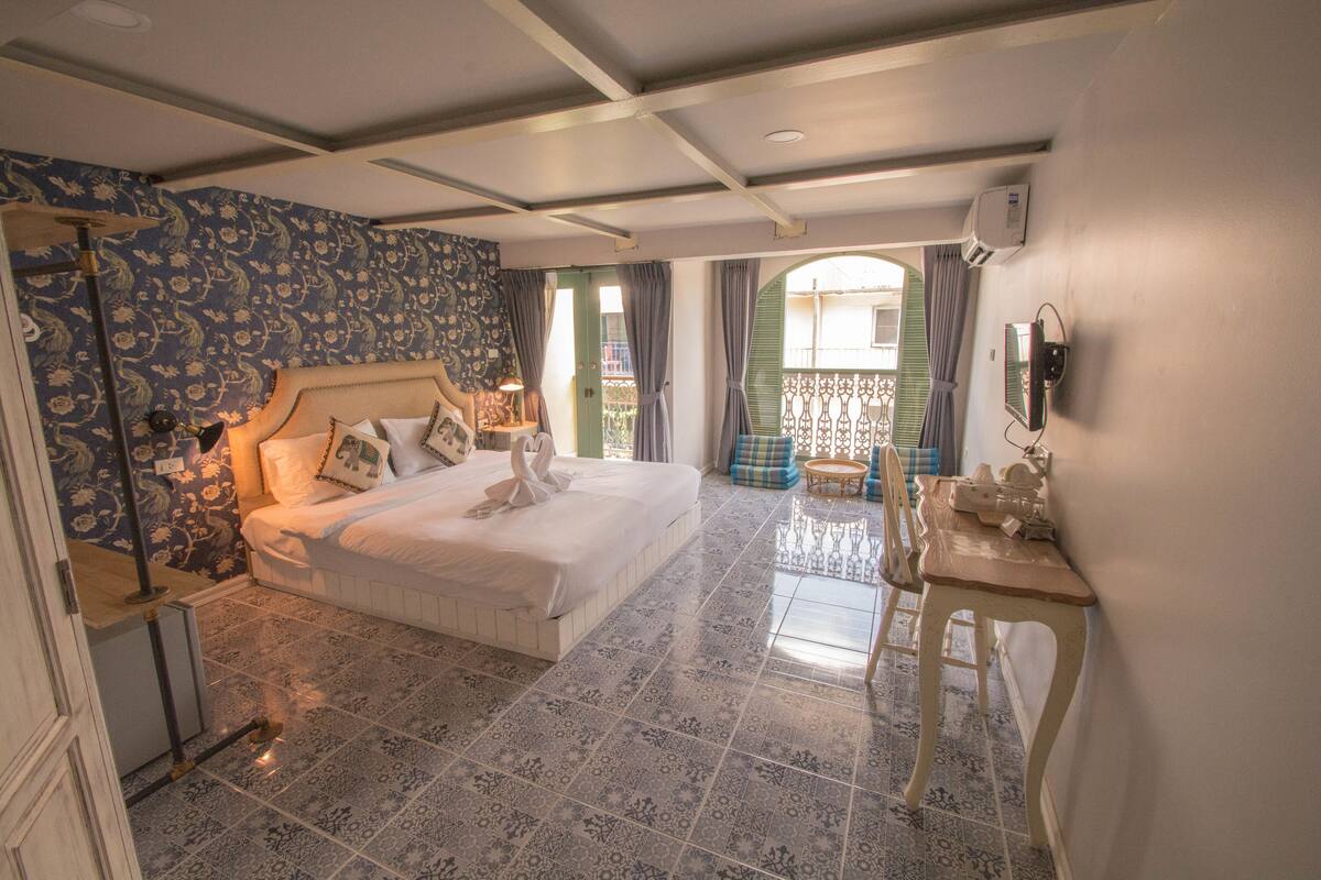 A hotel room with a large bed, a desk, a chair, and a balcony with a view.