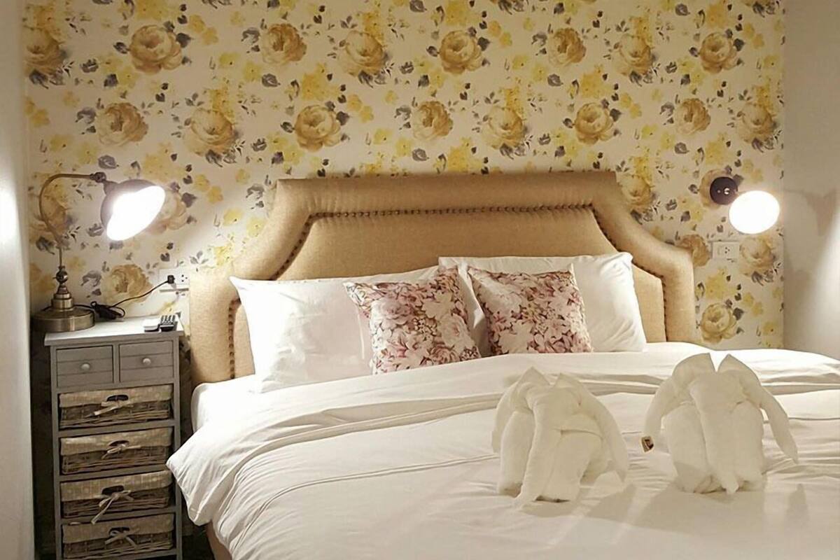 A neatly made bed with white bedding and two white stuffed animals on it.