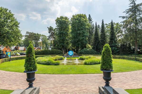 Un jardin aménagé avec une fontaine, des haies taillées avec soin et un panneau indiquant un espace de stationnement.