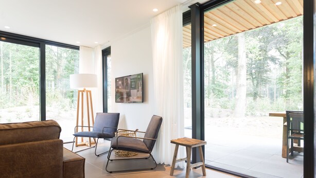 Una sala de estar moderna con un ventanal grande, un sofá, una silla, una mesita y una lámpara.