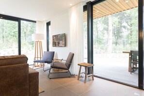 A modern living room with a large window, a sofa, a chair, a small table, and a lamp. - TopParken Landgoed de Scheleberg (Lunteren)