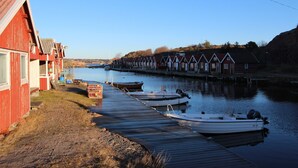 Una hilera de casas de madera rojas a orillas de un río tranquilo, con barcos amarrados al muelle.