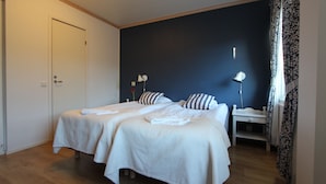 Cama doble con ropa de cama blanca, mesita de noche con lámpara y pared de acento azul oscuro.