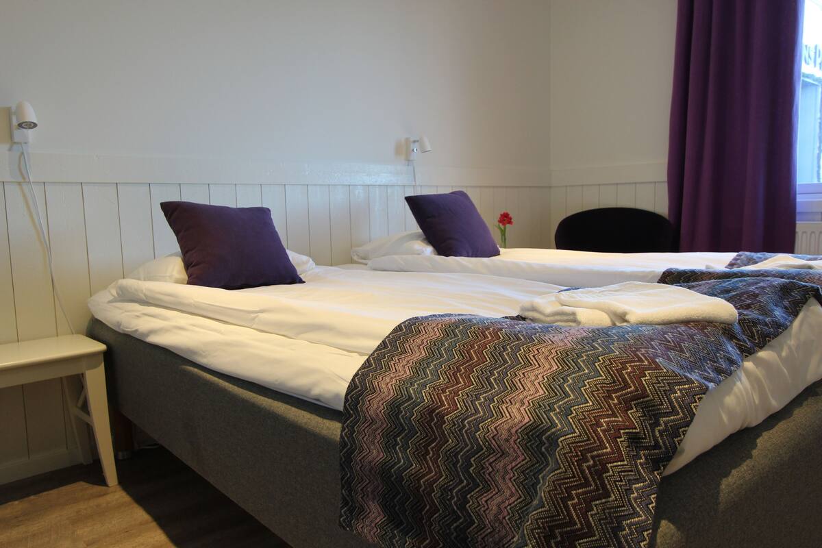 A double bed with white bedding and two purple pillows.