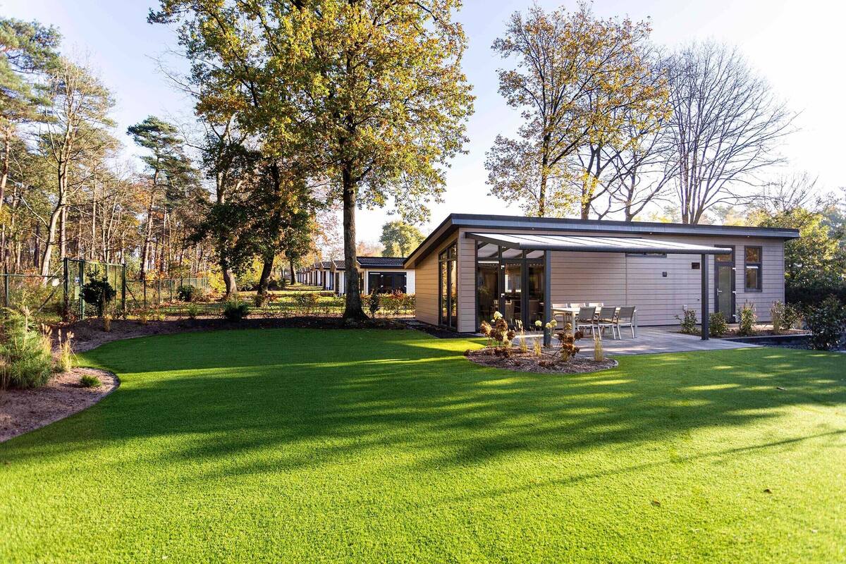 A modern house with a covered patio, a well-maintained lawn, and surrounding trees.
