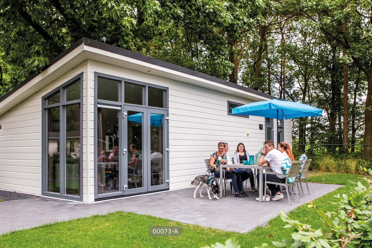 A modern outdoor seating area with a glass enclosure, a blue umbrella, and a grassy lawn.