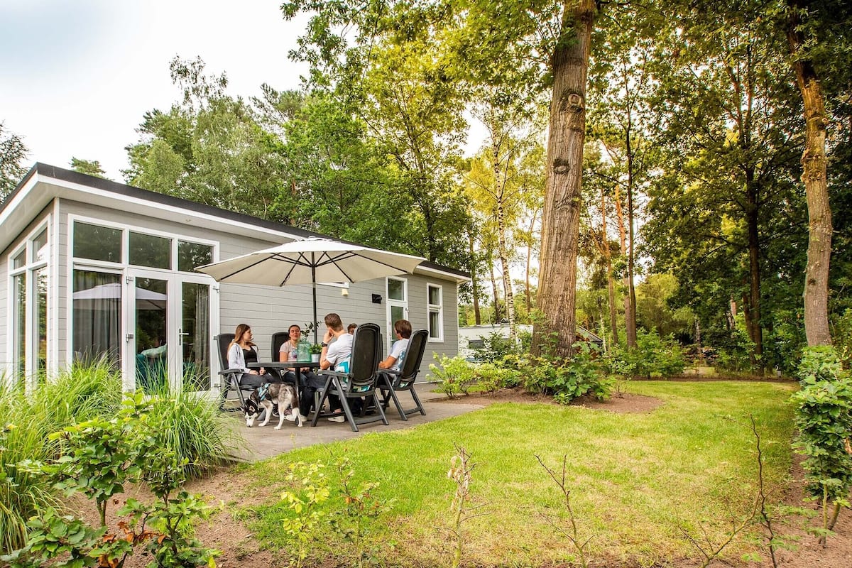 A modern house with a patio area where people are seated under an umbrella.