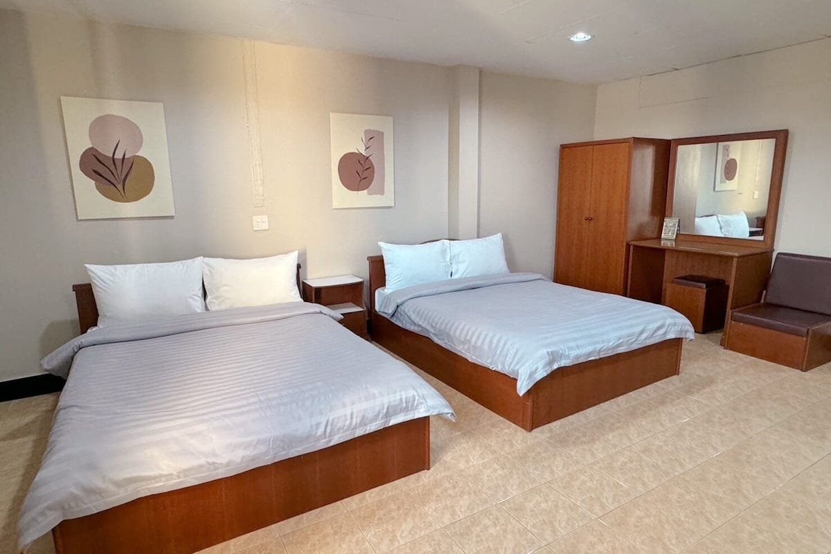 Habitación de hotel con dos camas, un armario de madera, un escritorio con una silla y obras de arte en las paredes.