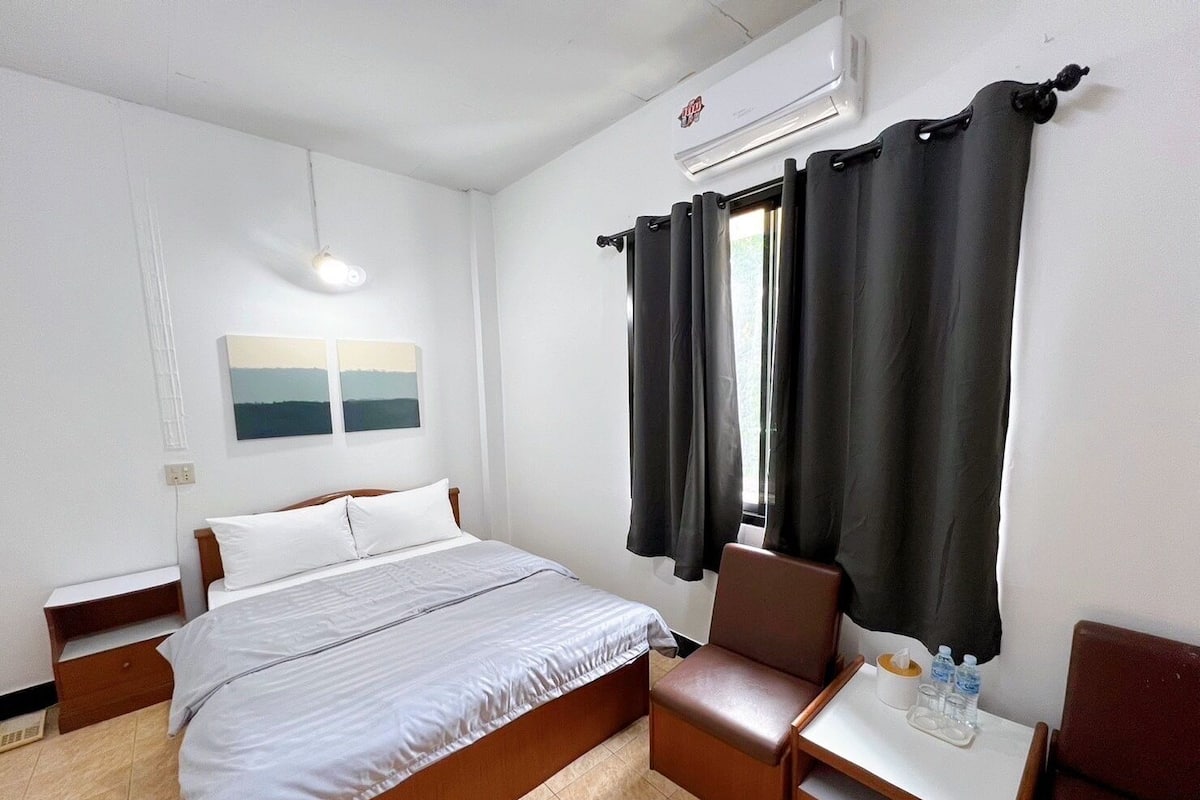 Habitación de hotel con cama, una silla, una mesita con botellas de agua y una ventana con cortinas.