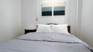 A bedroom with a bed, white walls, and two paintings on the wall. - Tokyo Hotel Korat (Nakhon Ratchasima)