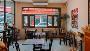 A restaurant interior with tables and chairs, large windows with a view of the street, and a sign on the wall. - Tokyo Hotel Korat (Nakhon Ratchasima)