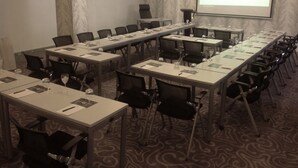 Una sala conferenze con lunghe tavolate e sedie, uno schermo proiettore che mostra “STAYWELL HOTELS” e una moquette fantasia.