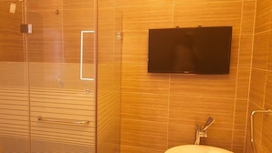 Un bagno con cabina doccia in vetro, un water e televisore a parete.