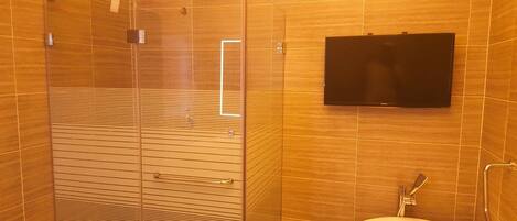 A bathroom with a glass shower enclosure, a toilet, and a mounted television.