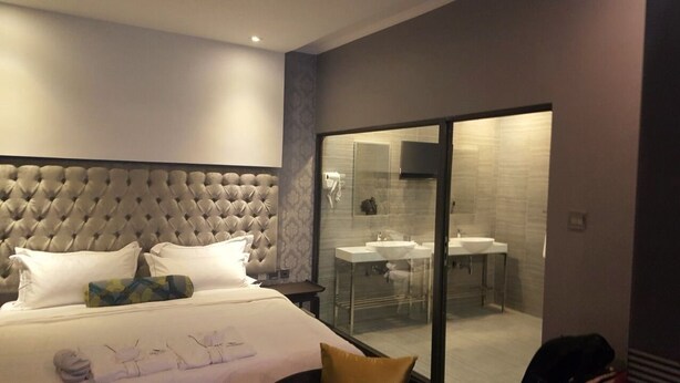 Camera d'hotel moderna con un'elegante testiera trapuntata, un letto grande, un bagno con cabina doccia in vetro e vista sul bagno attraverso una porta in vetro.