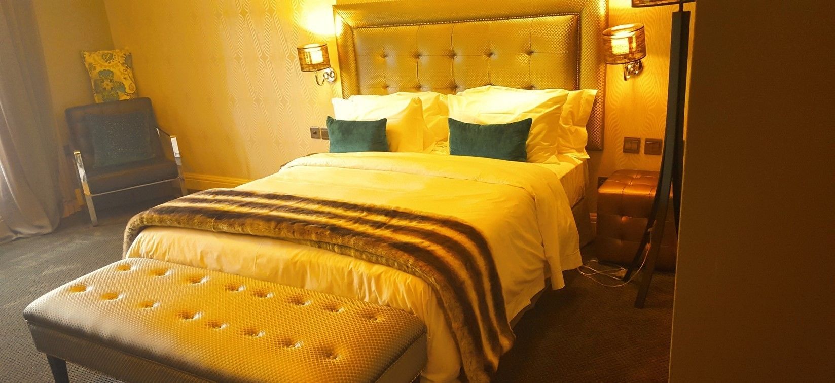 A hotel room with a large bed, a bench at the foot of the bed, and two wall-mounted lamps.