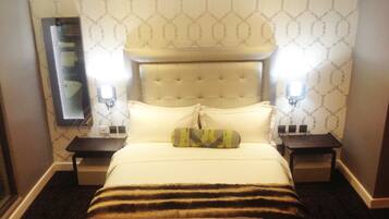 Una habitación de hotel con una cama grande, dos mesitas de noche, un cabecero y una lámpara fijada a la pared.