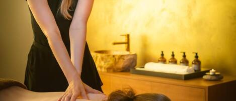 A massage therapy session in a room with a wooden cabinet and shelves containing bottles.