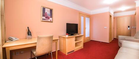 A hotel room with a desk, chair, television, and a sofa.