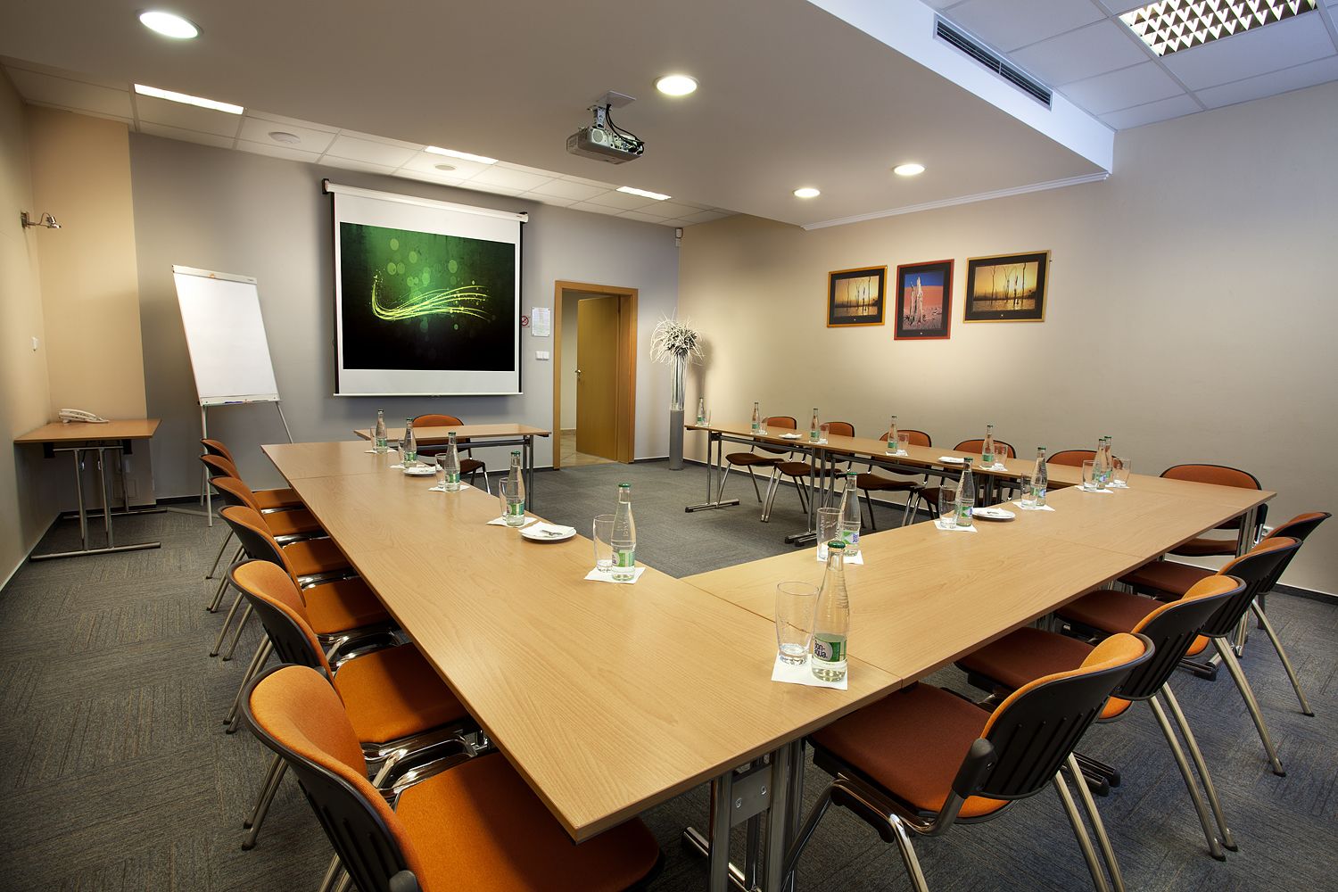 Une salle de conférence avec une longue table, des chaises, un projecteur, un tableau blanc et des tableaux encadrés accrochés au mur.