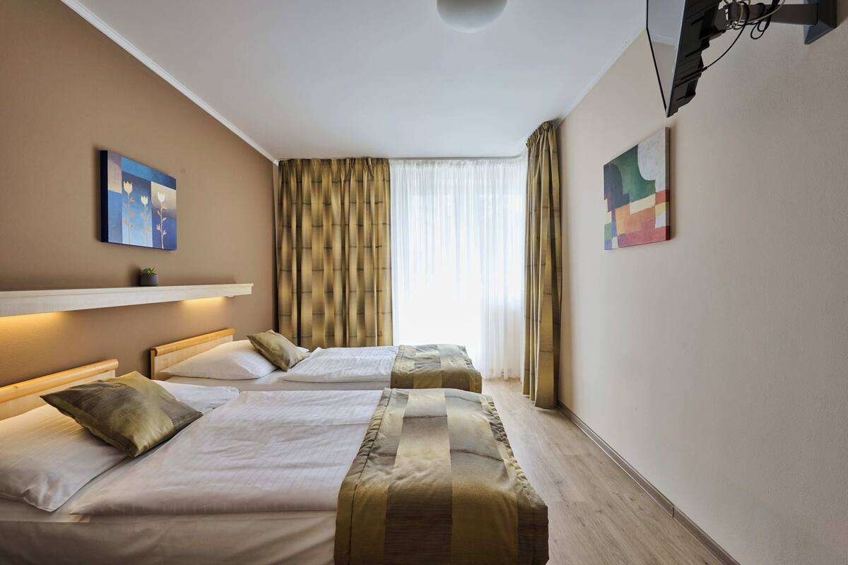 Una habitación de hotel con dos camas, un ventanal con cortinas y obras de arte en las paredes.
