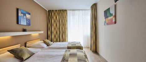 A hotel room with two beds, a large window with curtains, and artwork on the walls.
