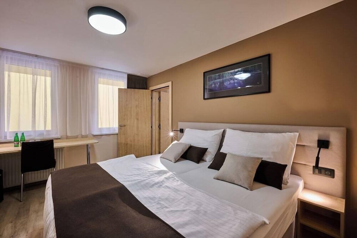 Una habitación de hotel con cama, mesita de noche, lámpara y un cuadro en la pared.