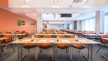 A conference room with multiple tables and chairs, equipped with projectors and screens, and decorated with framed pictures on the walls.