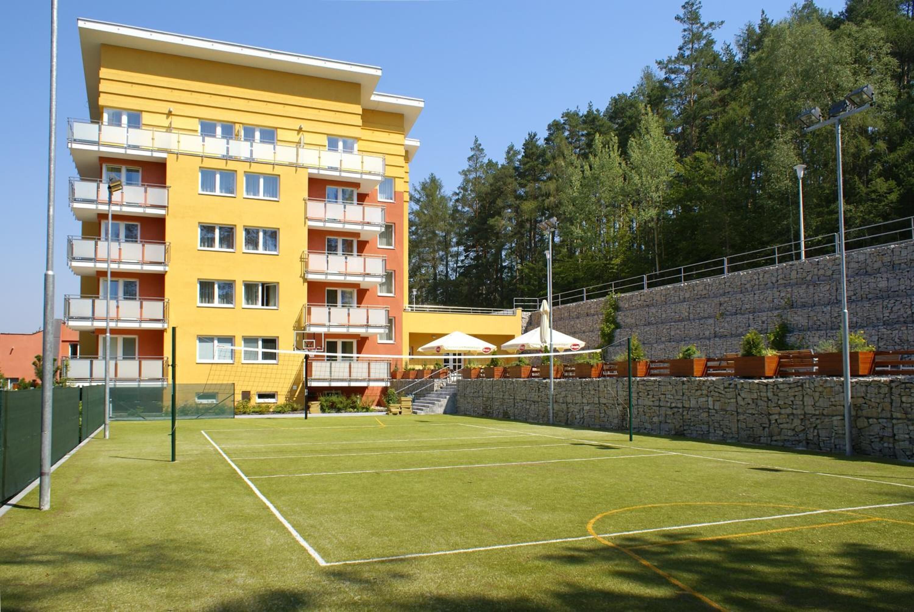 Ein Tennisplatz mit Netz, umgeben von einer Steinmauer und einem gelben Gebäude mit Balkonen.