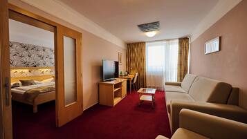 A hotel room with a bed, a TV, a desk, a sofa, and a red carpet.
