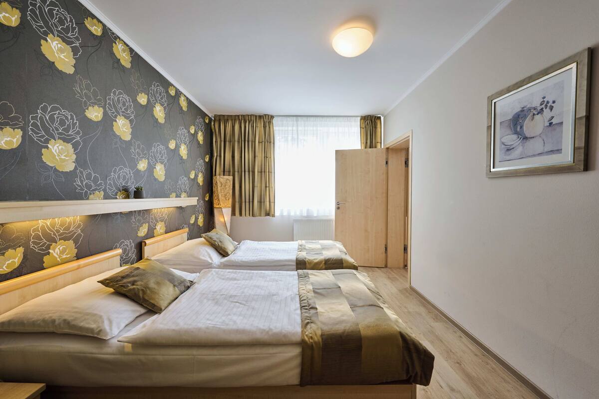 Habitación de hotel con dos camas, un ventanal con cortinas, un armario de madera y un cuadro en la pared.