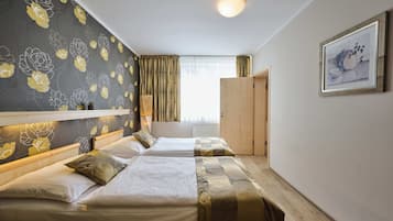 A hotel room with two beds, a large window with curtains, a wooden wardrobe, and a framed picture on the wall.