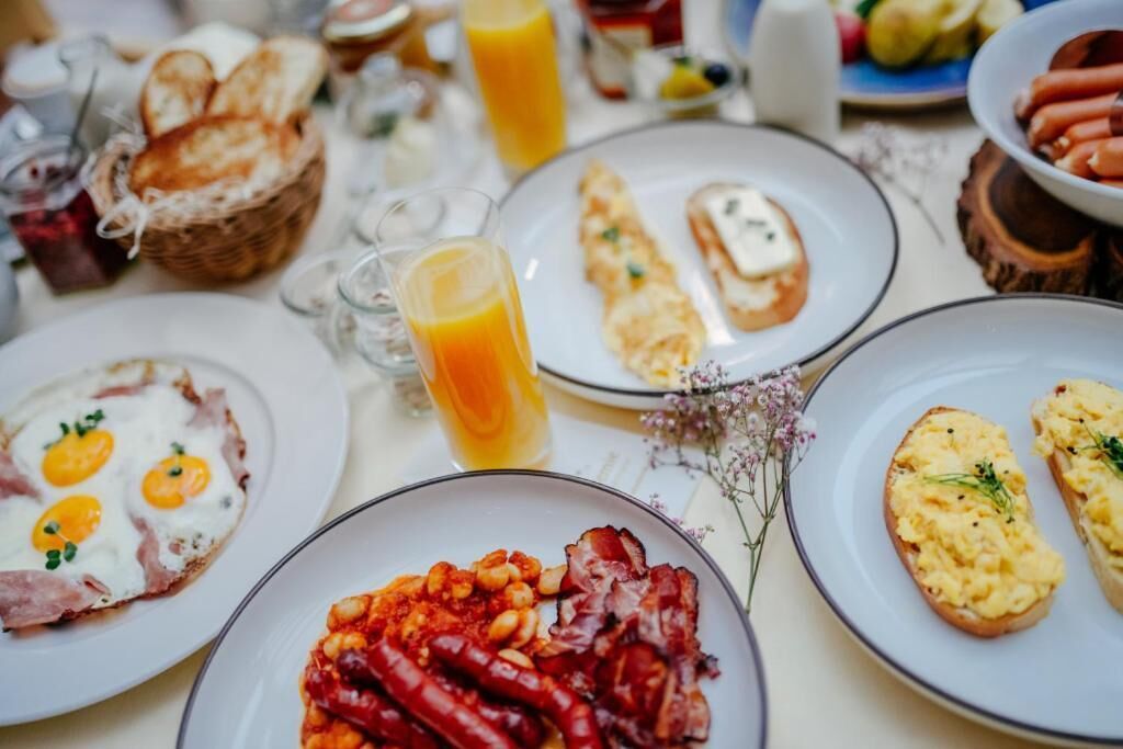 A breakfast table with various dishes including eggs, bacon, beans, toast, and a glass of orange juice.