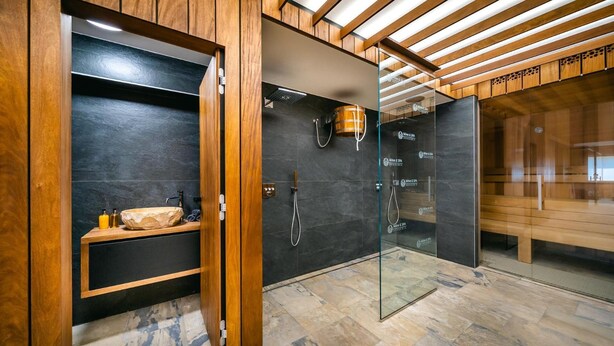 A modern bathroom with a wooden vanity, a glass shower enclosure, and a stone-tiled floor.
