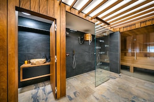 Un baño moderno con tocador de madera, cabina de ducha con mampara de vidrio y suelo de baldosas de piedra.