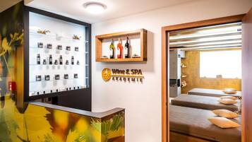 A spa area with a reception desk displaying various products, a wall-mounted sign for 'Wine & SPA ACADEMIE', and a relaxation area with beds and pillows.