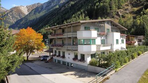 Un hôtel à plusieurs étages, doté de balcons, situé dans une région montagneuse et disposant d’un parking à l’avant.