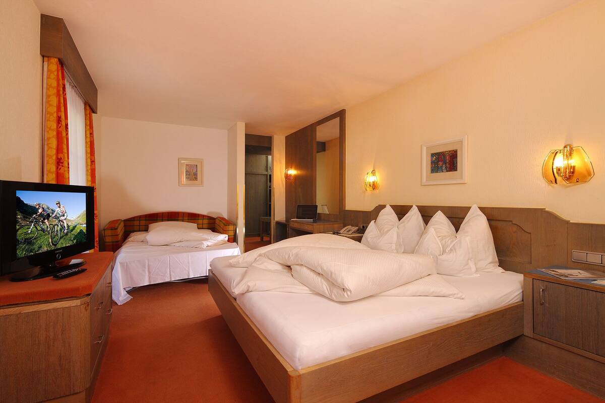 Ein Hotelzimmer mit einem großen Bett, einem kleineren Bett, einem Fernseher, einem Schreibtisch und einem Kleiderschrank.