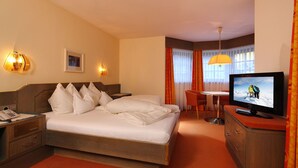 Une chambre d’hôtel comprenant un lit, un bureau avec un téléphone, une télévision et un coin repas avec une table et des chaises.