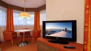 Une chambre d’hôtel avec une télévision diffusant un paysage de montagne, une table à manger avec des chaises et une télécommande posée sur la commode.