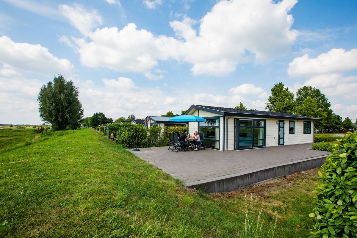 Ein modernes Haus mit einer Terrassenfläche, auf der zwei Personen an einem Tisch sitzen.
