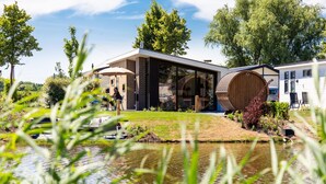 Una casa moderna con un barril de madera grande, una puerta de cristal y un área verde al frente.