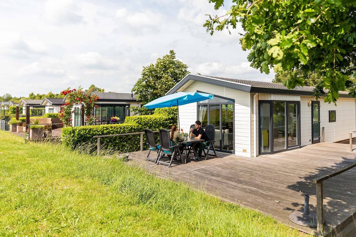 Ein moderner Außenbereich mit Holzterrasse, blauem Sonnenschirm und einem gläsernen Gebäude.