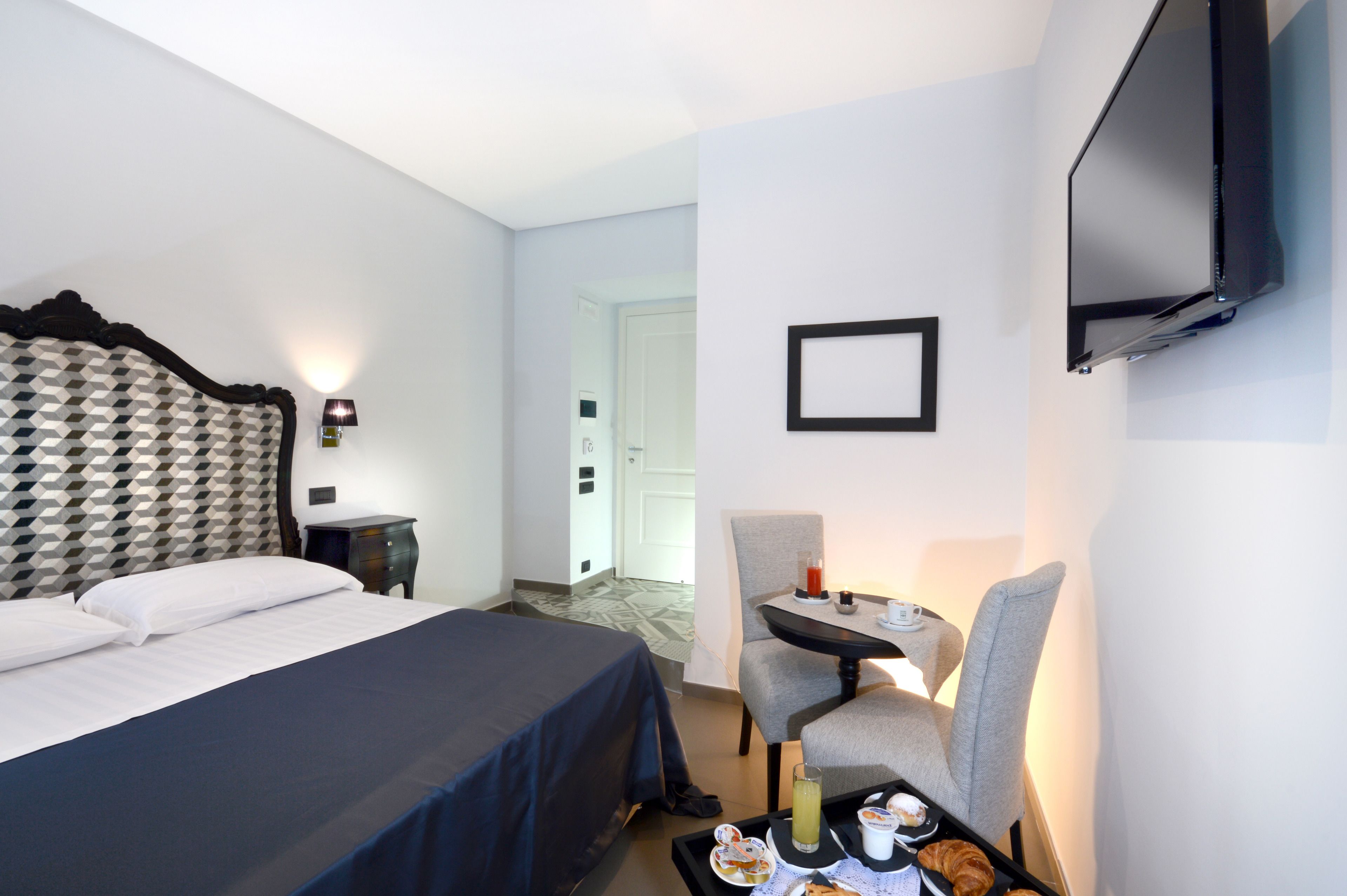 A hotel room with a bed, a desk with a chair, a television, and a tray with food and drinks.