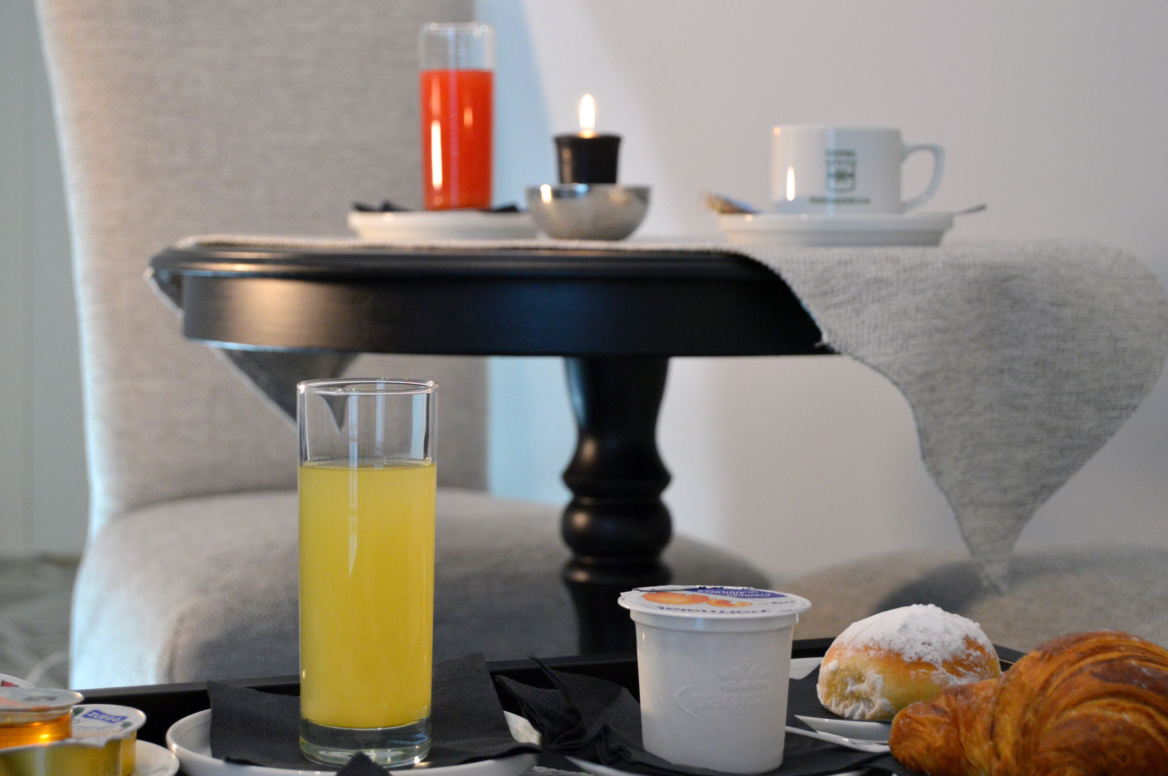 Un plateau de petit-déjeuner avec un verre de jus d’orange, un croissant, une pâtisserie, une tasse de café et une bougie, le tout posé sur une table.