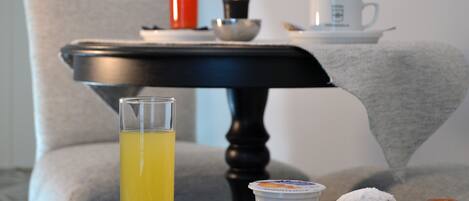 Un plateau de petit-déjeuner avec un verre de jus d’orange, un croissant, une pâtisserie, une tasse de café et une bougie, le tout posé sur une table.