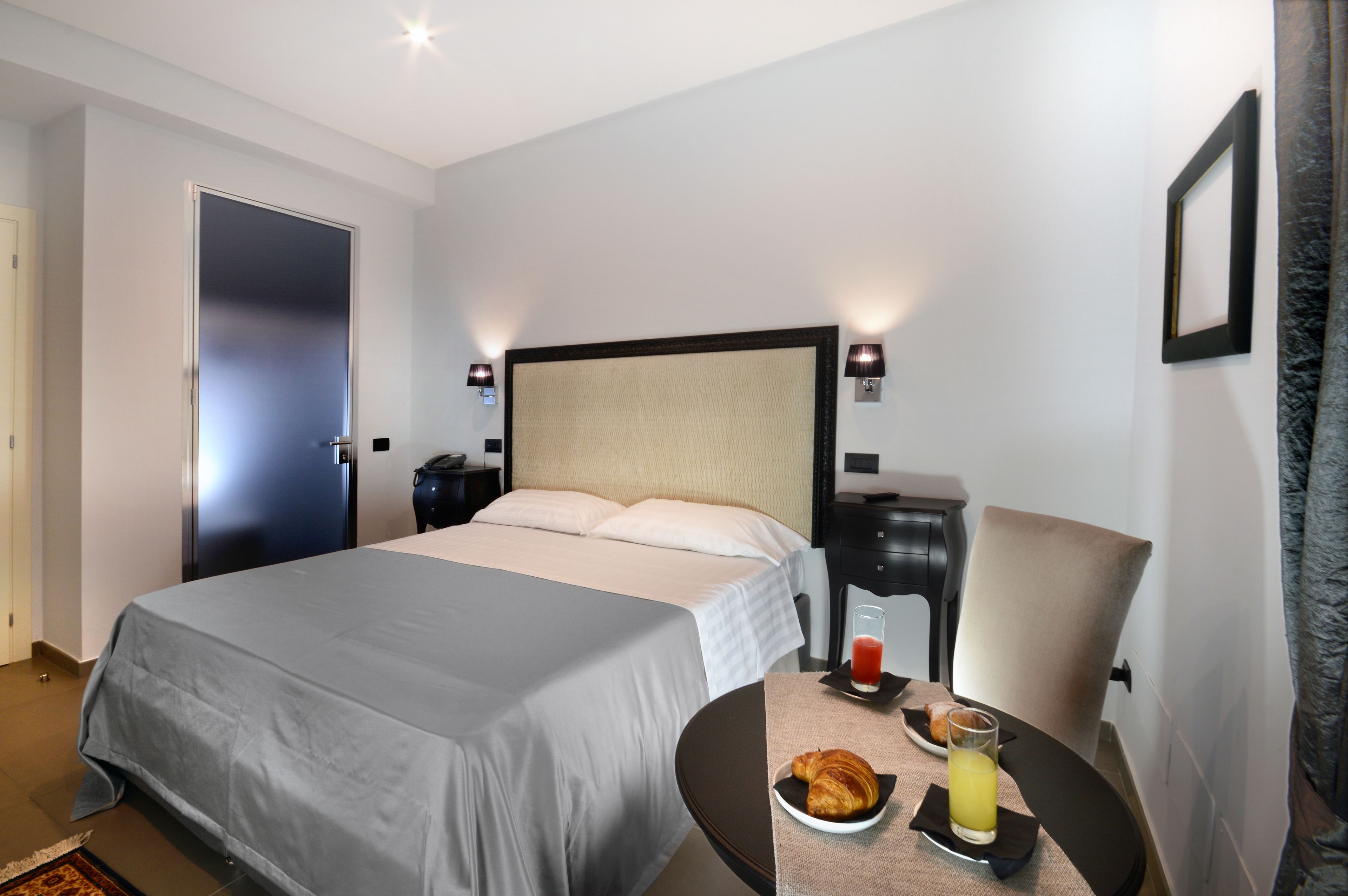 A hotel room with a bed, bedside table, chair, and a small dining table with breakfast items.